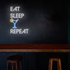 LED Neon nápis 'Eat sleep drink repeat' nad stolem v baru- Ideální pro milovníky koktejlů a drinků